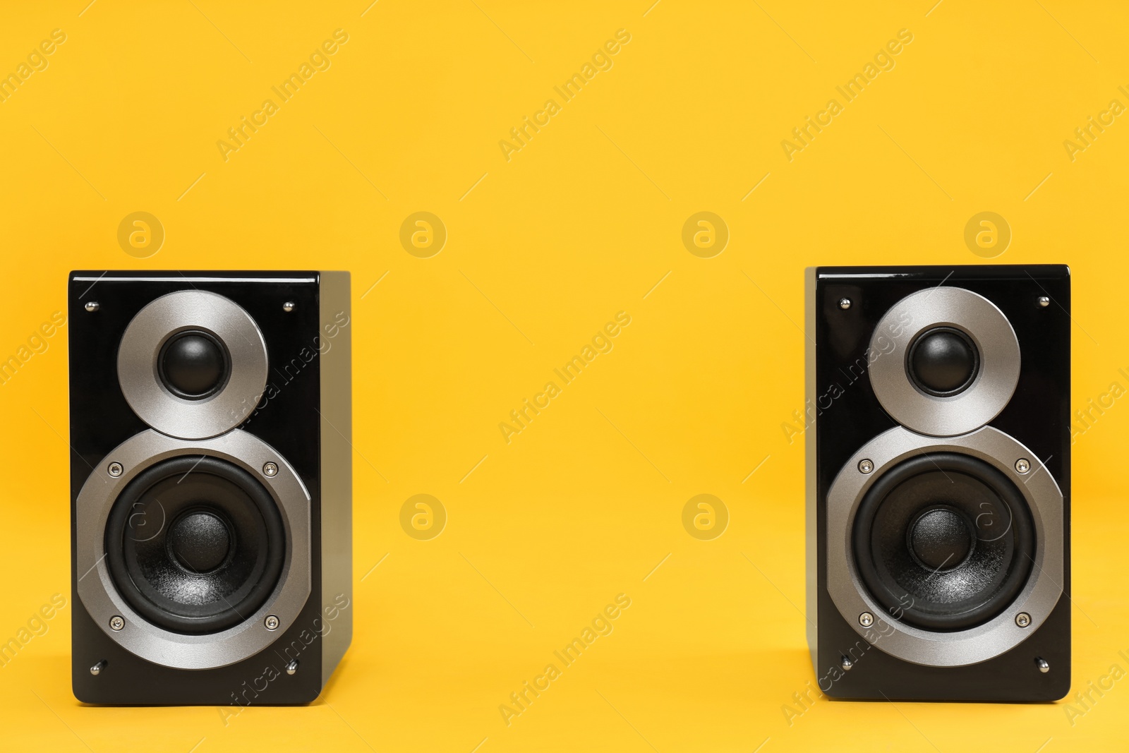 Photo of Modern powerful audio speakers on yellow background, space for text