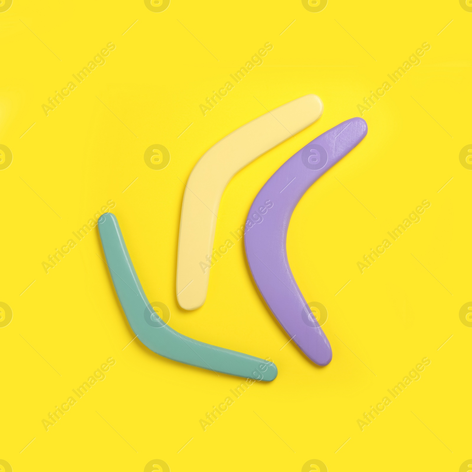 Photo of Colorful wooden boomerangs on yellow background, flat lay. Space for text