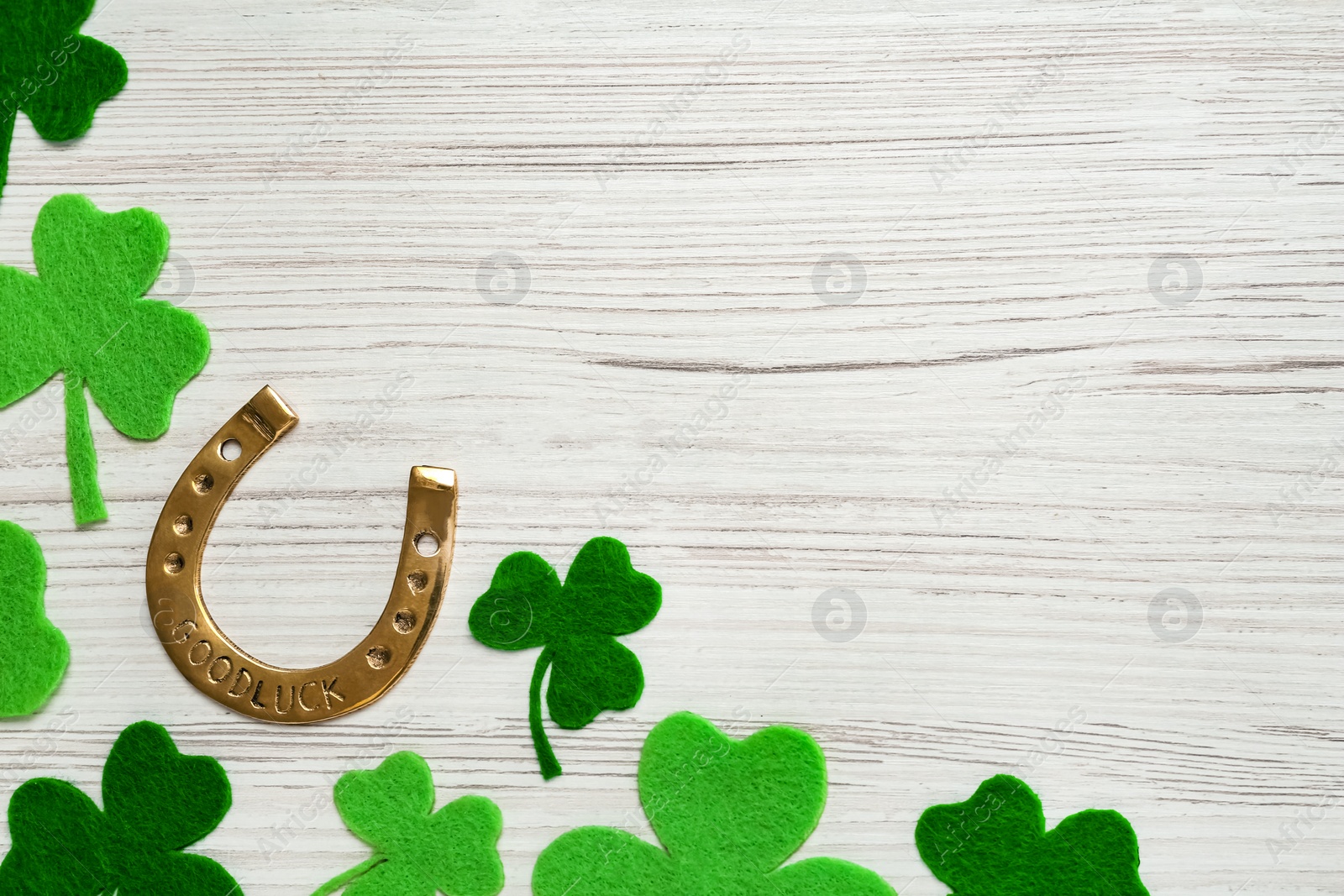 Photo of Golden horseshoe and decorative clover leaves on white wooden table, flat lay with space for text. Saint Patrick's Day celebration