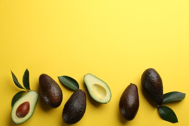 Photo of Whole and cut ripe avocadoes with green leaves on yellow background, flat lay. Space for text