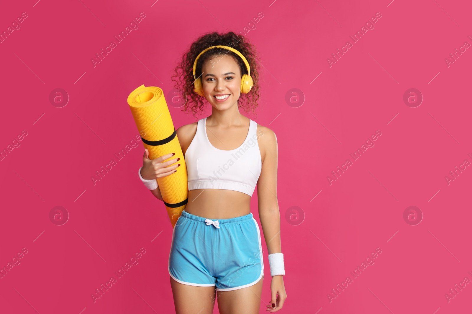 Photo of Beautiful African American woman with yoga mat and headphones on pink background