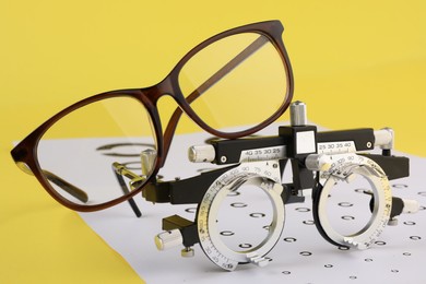 Photo of Vision test chart and glasses on yellow background, closeup