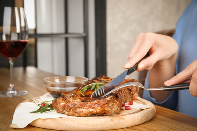 Photo of Woman eating delicious grilled ribs at wooden table indoors, closeup