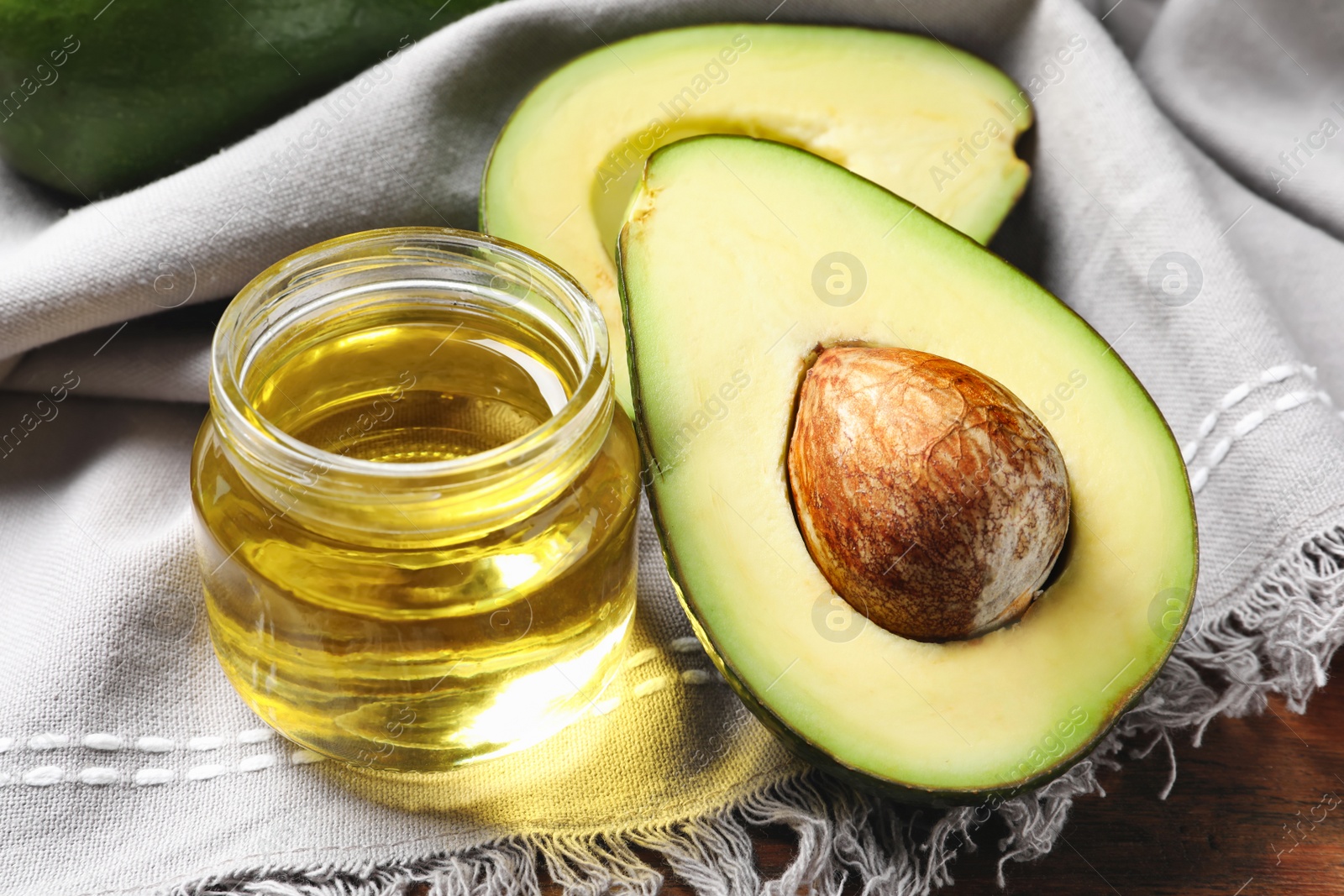 Photo of Jar with oil and ripe fresh avocado on table, closeup