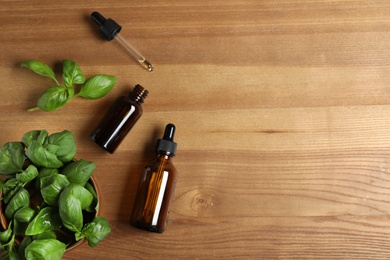 Flat lay composition with bottles of essential oil, basil and space for text on wooden background