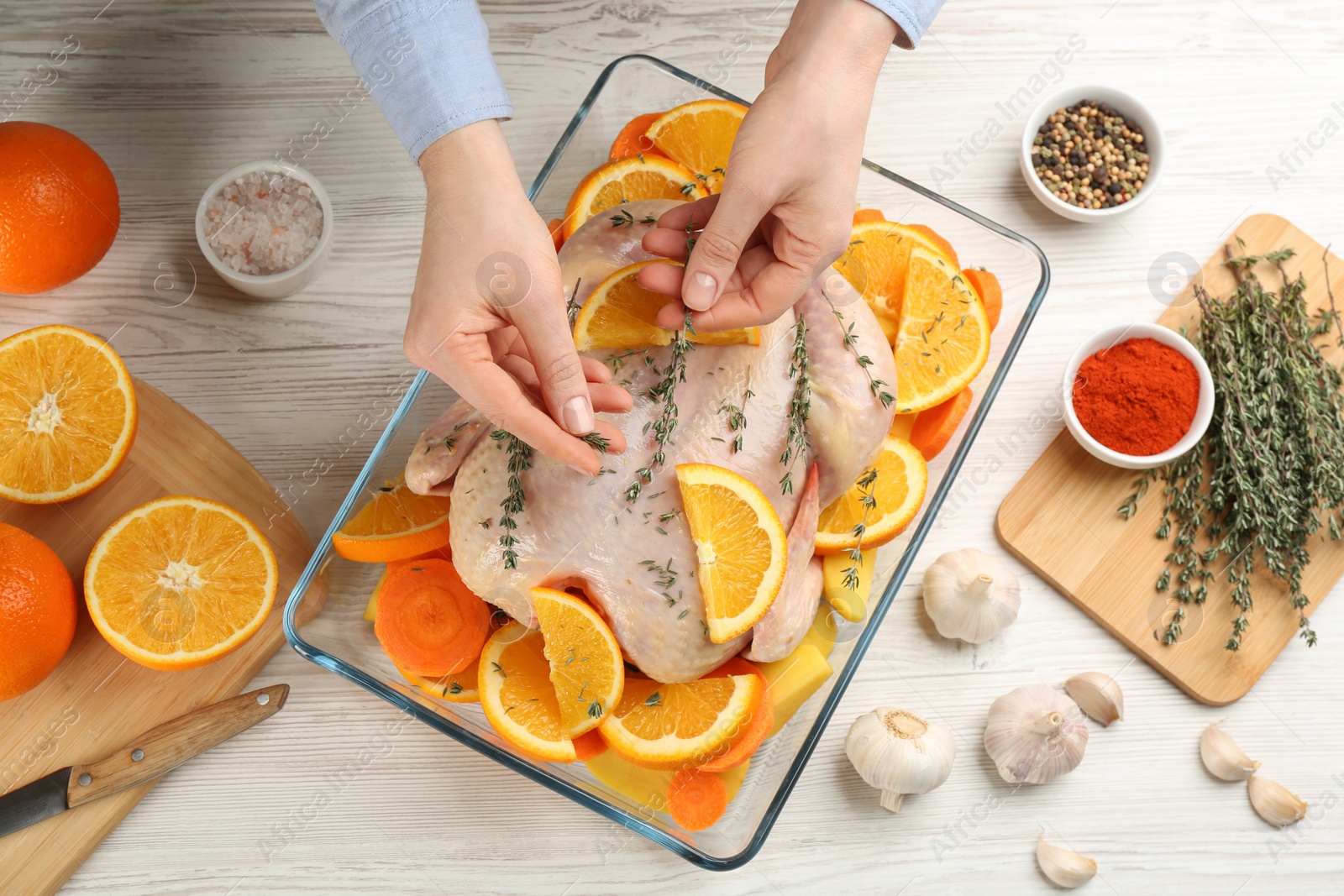 Photo of Woman adding thyme to raw chicken with orange slices at white wooden table, top view