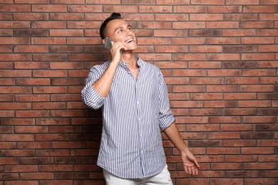 Photo of Young man talking on phone against brick wall