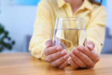 Photo of Woman holding glass of water at wooden table, closeup with space for text. Refreshing drink