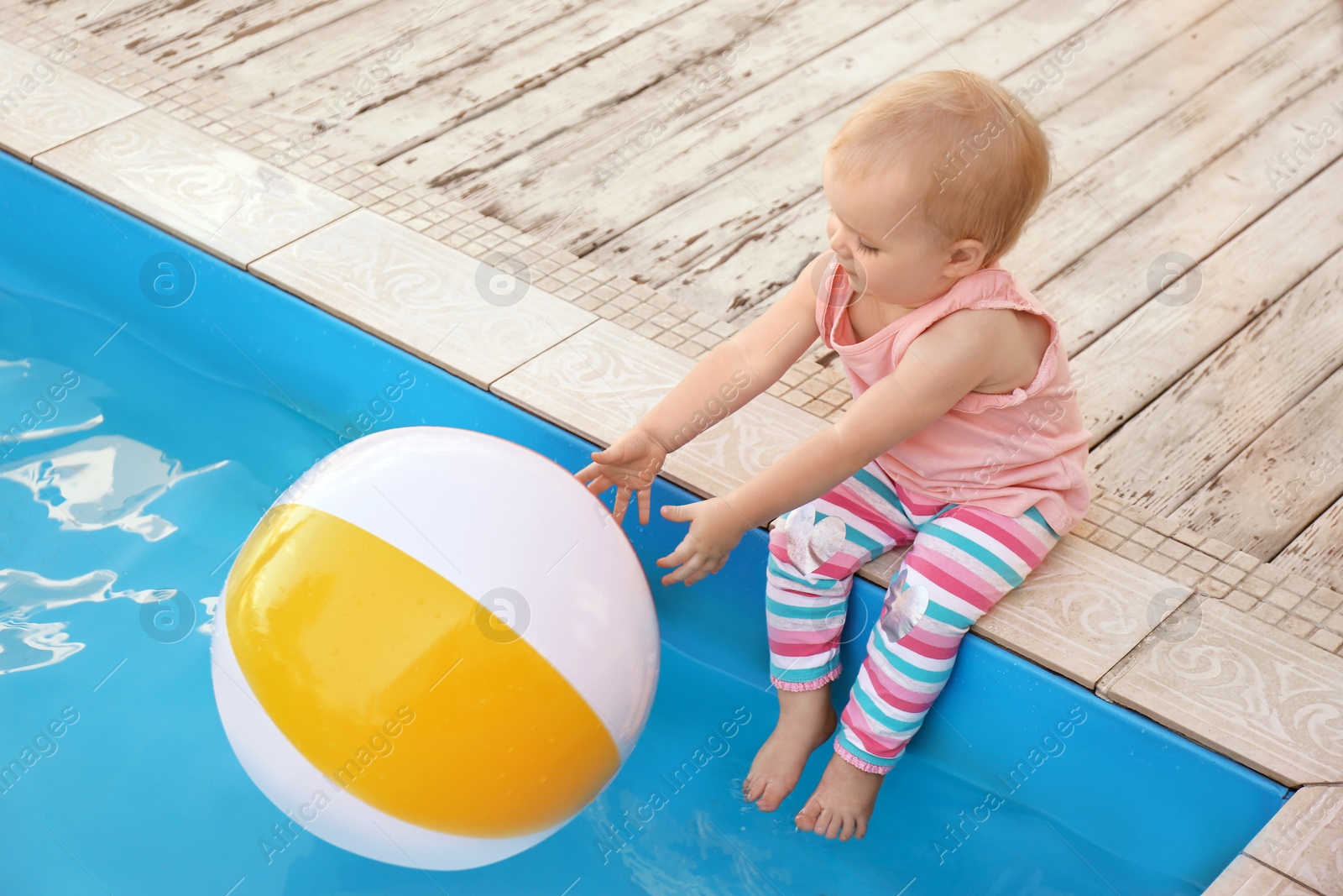 Photo of Little baby reaching for inflatable ball at outdoor swimming pool. Dangerous situation