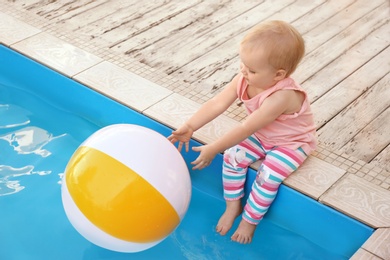 Photo of Little baby reaching for inflatable ball at outdoor swimming pool. Dangerous situation