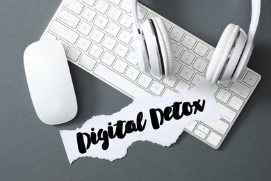 Paper note with phrase DIGITAL DETOX, headphones and computer devices on grey background, flat lay