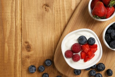 Photo of Yogurt served with berries on wooden table, top view. Space for text