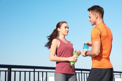 Photo of Young sporty couple with bottles of water outdoors on sunny day. Space for text