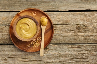 Photo of Spoon and bowl of tasty mustard sauce with dry seeds on wooden table, top view. Space for text