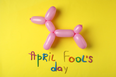 Photo of Balloon animal and phrase APRIL FOOL'S DAY on yellow background, flat lay