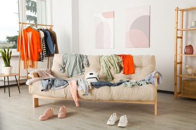 Photo of Messy pile of clothes on sofa and shoes in living room