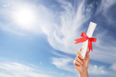 Image of Graduated student holding diploma against blue sky on sunny day, closeup