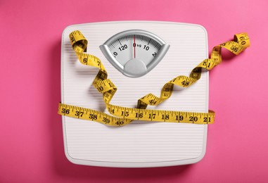 Photo of Weight loss concept. Scales and measuring tape on pink background, top view