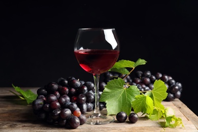 Photo of Fresh ripe juicy grapes and glass of red wine on table against black background