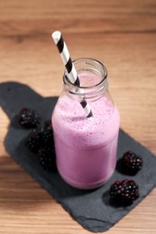 Delicious blackberry smoothie in glass bottle with straw and fresh berries on wooden table