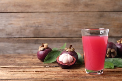 Photo of Delicious fresh mangosteen juice in glass on wooden table, space for text