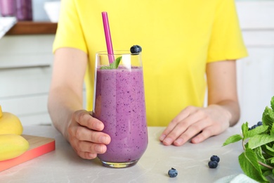 Photo of Woman holding glass of delicious blueberry smoothie at table in kitchen, closeup