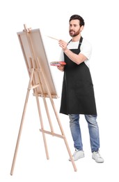 Photo of Artist with brush painting against white background. Using easel to hold canvas