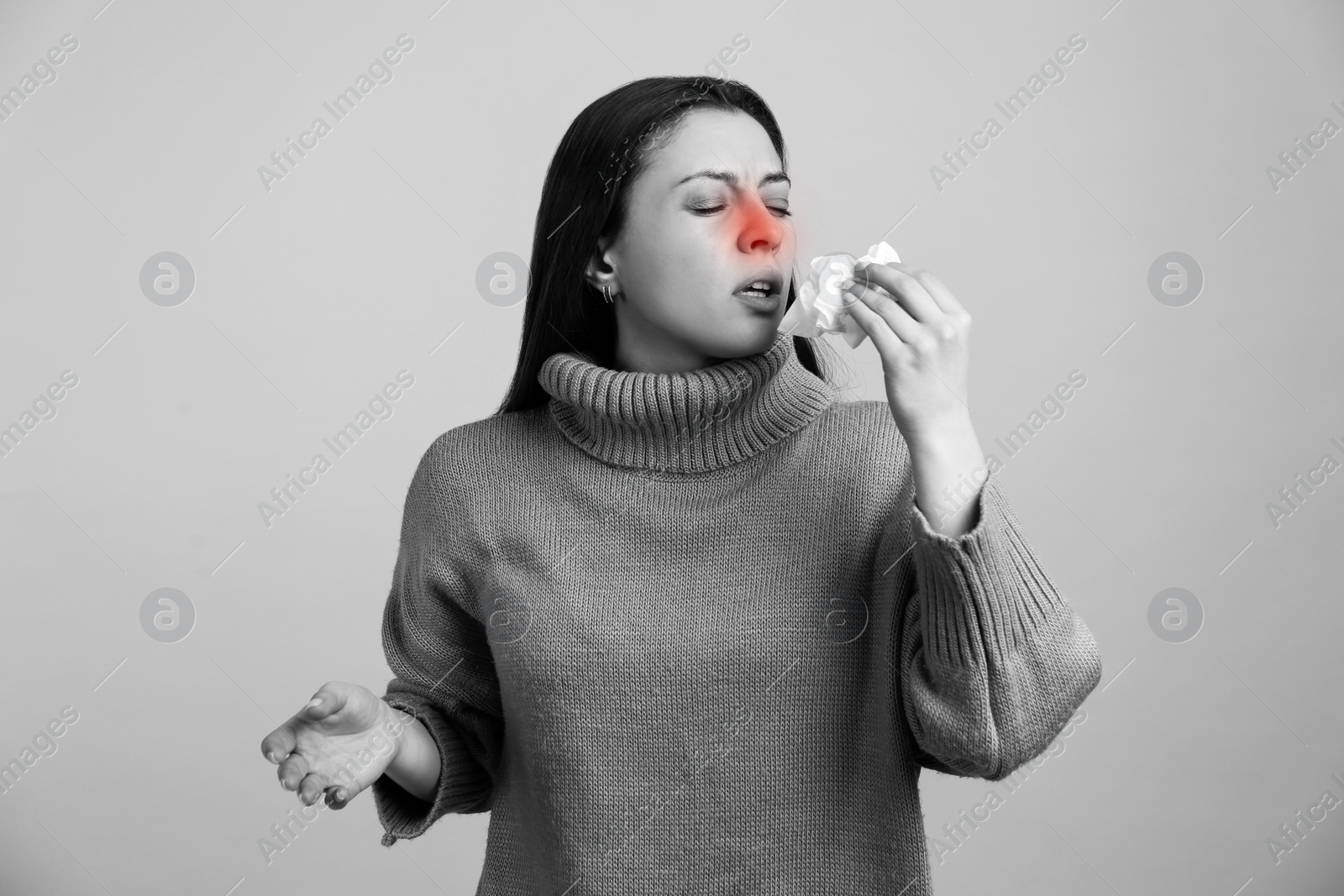 Image of Young woman with tissue sneezing on light background, toned in black and white. Runny nose