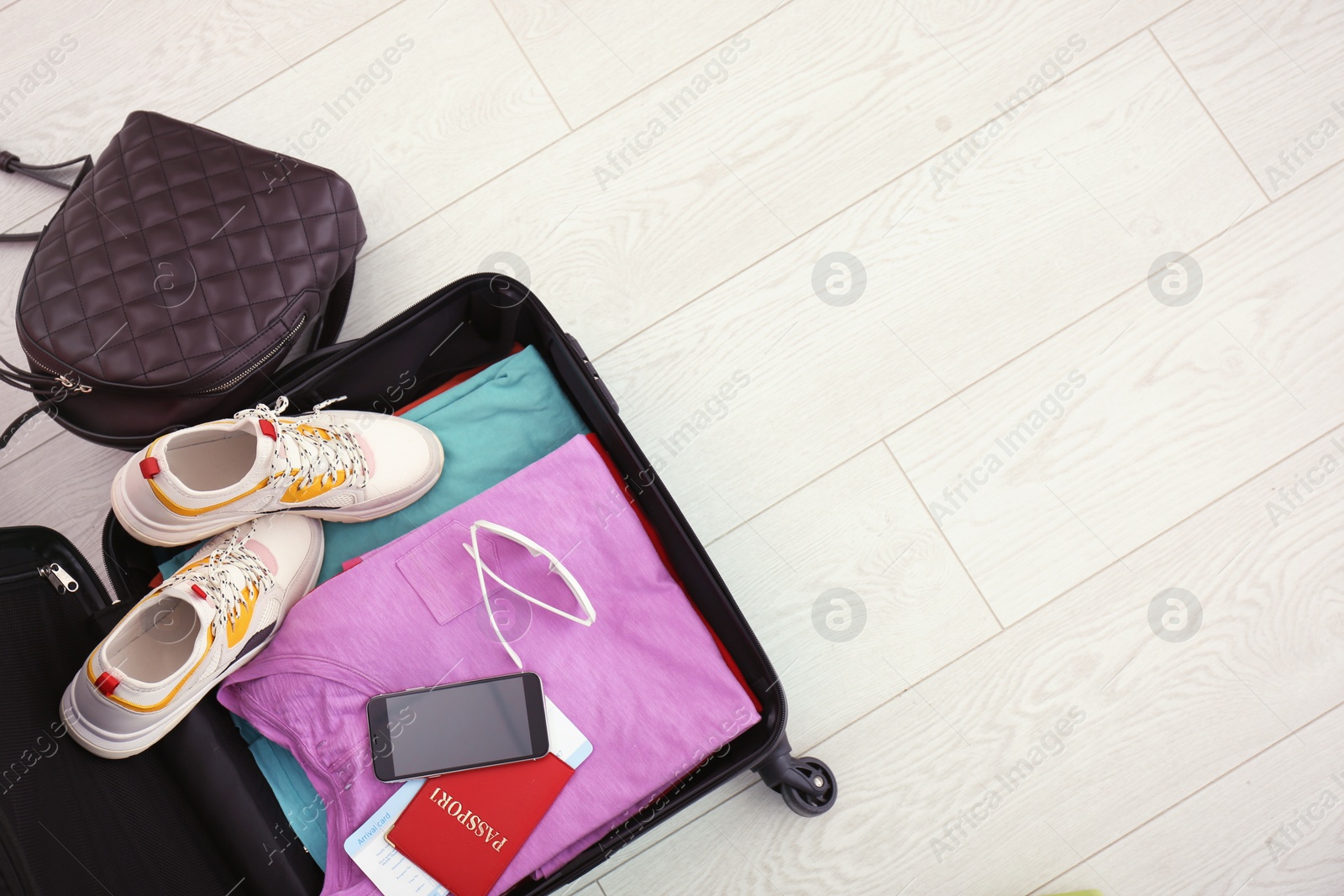 Photo of Modern suitcase full of clothes on wooden floor, top view with space for text
