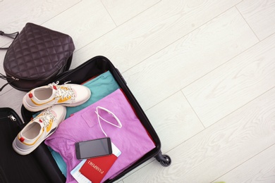 Modern suitcase full of clothes on wooden floor, top view with space for text