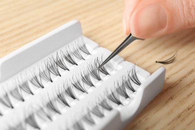 Photo of Woman holding tweezers with false eyelash, closeup