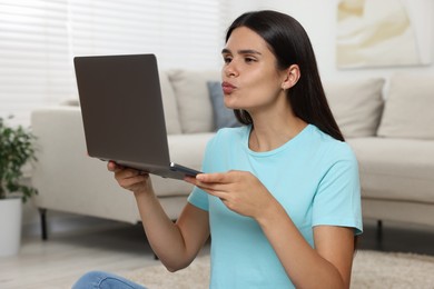 Photo of Young woman having video chat via laptop and blowing kiss at home