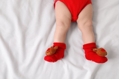 Baby wearing festive Christmas socks on white bedsheet, top view