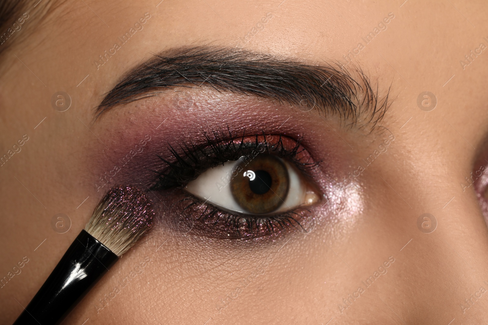 Photo of Applying dark eye shadow with brush onto woman's face, closeup. Beautiful evening makeup