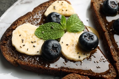 Photo of Tasty toast with banana, blueberries, honey and chia seeds on plate, closeup