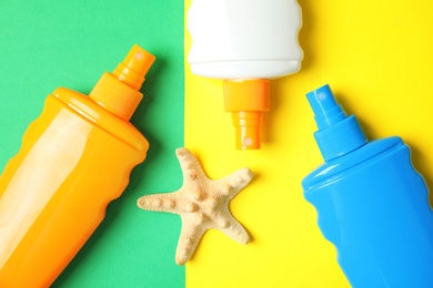 Photo of Bottles with sun protection products and starfish on color background, flat lay