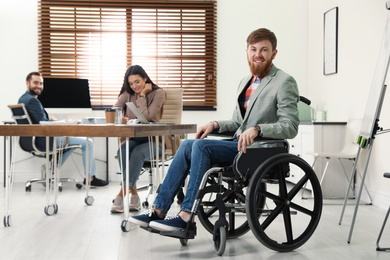 Photo of Young man in wheelchair with colleagues at office
