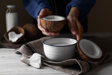 Photo of Woman holding nut with coconut milk at white wooden table, closeup