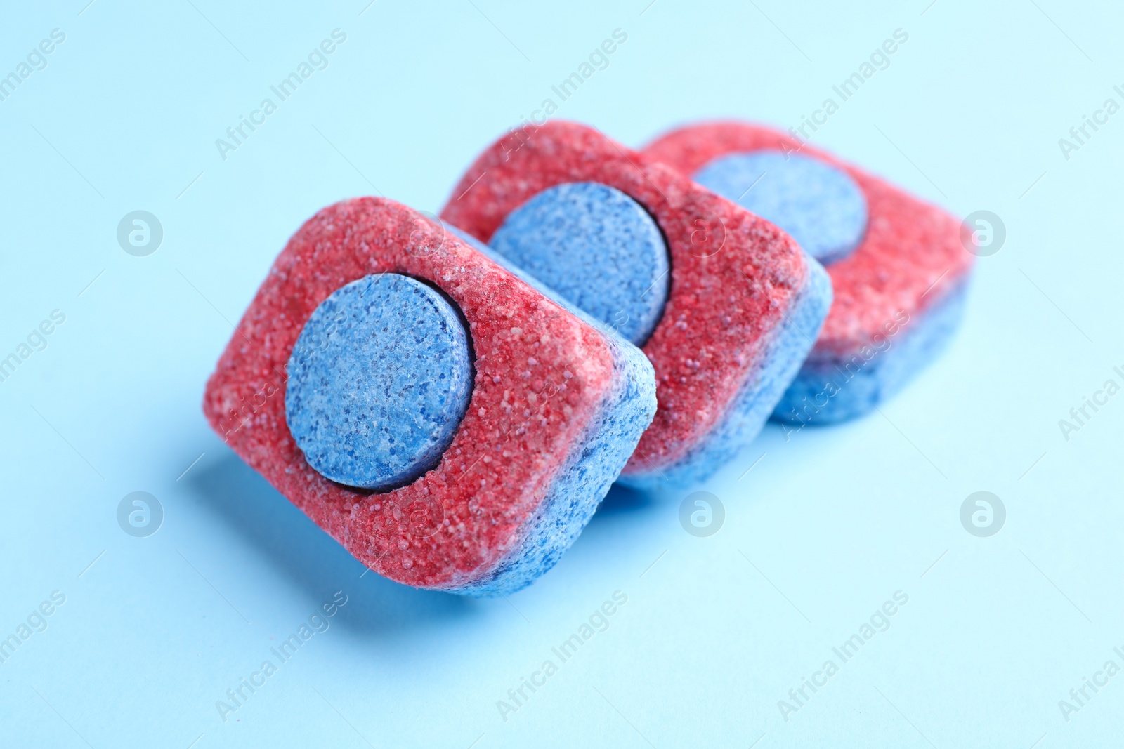 Photo of Dishwasher detergent tablets on light blue background, closeup