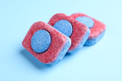 Photo of Dishwasher detergent tablets on light blue background, closeup