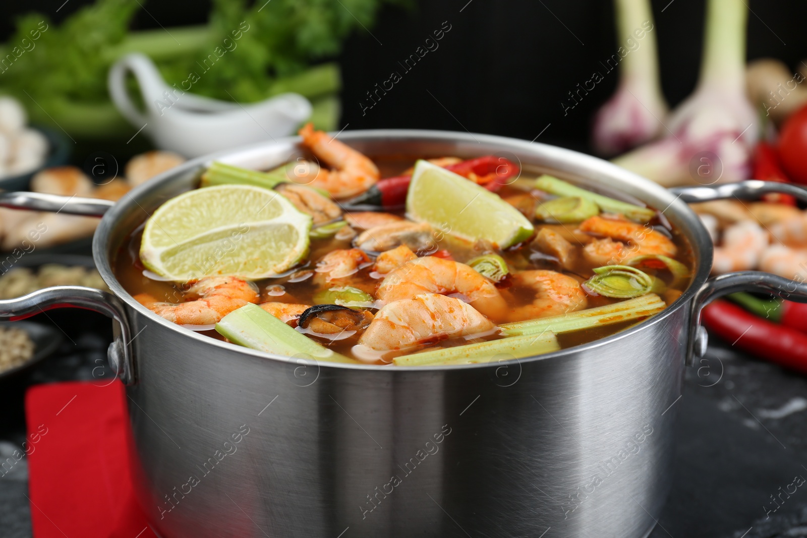 Photo of Saucepan with delicious Tom Yum soup and ingredients on table, closeup