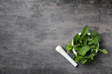 Mortar with fresh green herbs on grey background, top view