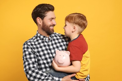 Photo of Father and his son with ceramic piggy bank on orange background