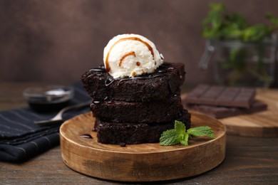 Photo of Tasty brownies served with ice cream and caramel sauce on wooden table, closeup