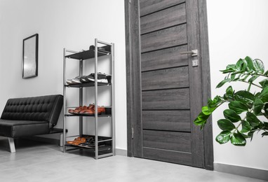 Photo of Shoe storage unit and stylish leather sofa near wooden door in hallway. Interior design