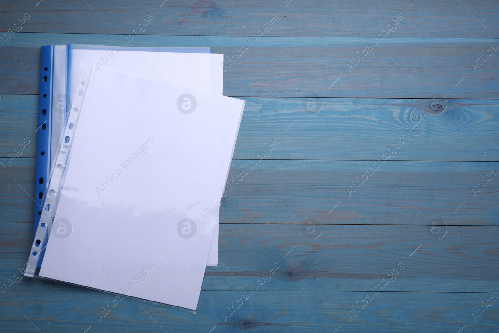 Photo of File folder with punched pockets and paper sheets on light blue wooden table, flat lay. Space for text