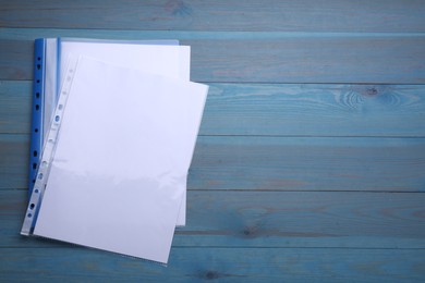 File folder with punched pockets and paper sheets on light blue wooden table, flat lay. Space for text