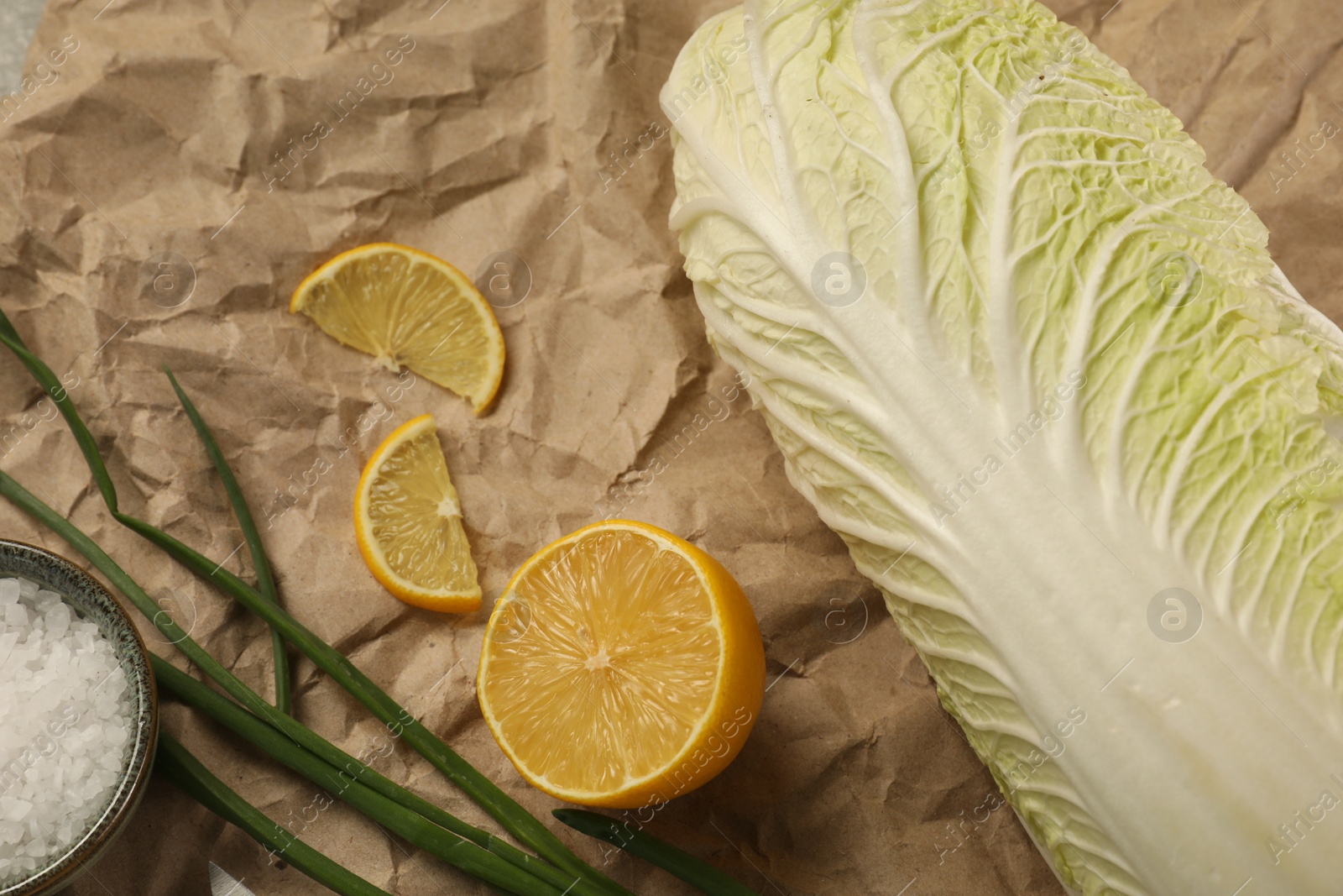 Photo of Fresh Chinese cabbage, lemon, green onion and salt on kraft paper, closeup