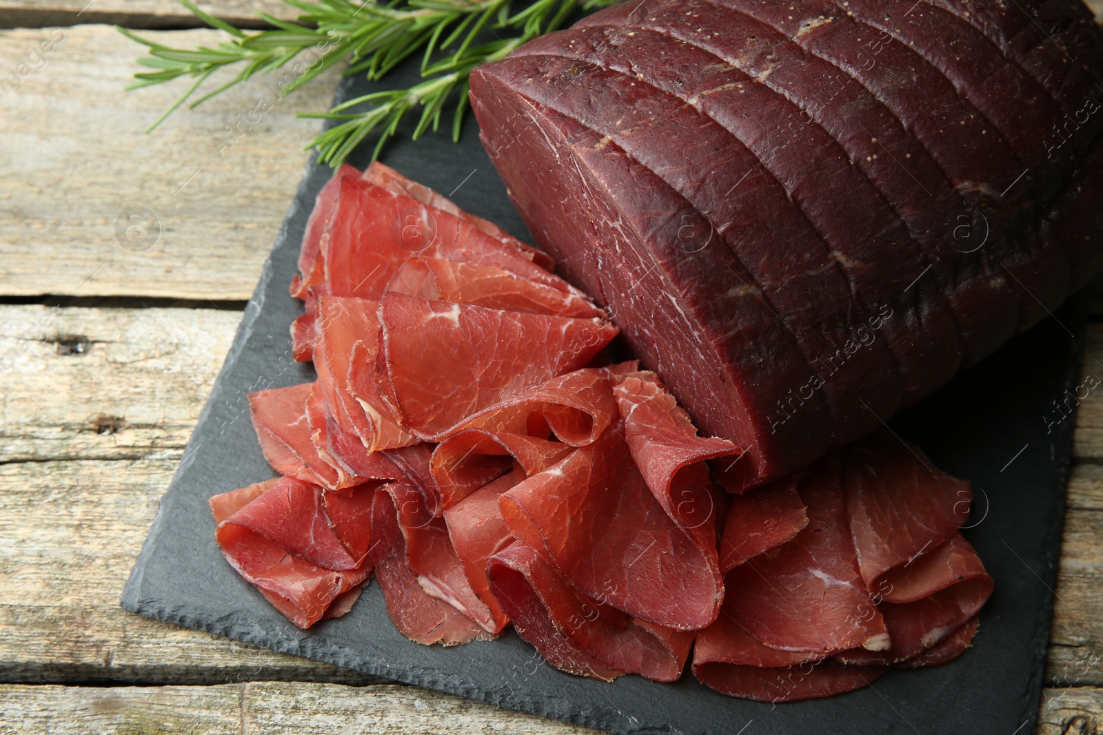 Photo of Tasty bresaola and rosemary on wooden table, closeup