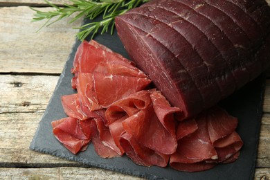 Tasty bresaola and rosemary on wooden table, closeup